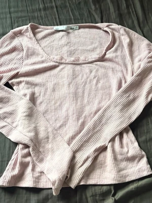 Ljusrosa ribbad långärmad topp - Supersöt ljusrosa ribbad topp från med lång ärm och fyrkantig ringning. Dekorerad med små blommor längs halsringningen. Perfekt att styla med jeans eller kjol för en chill look.