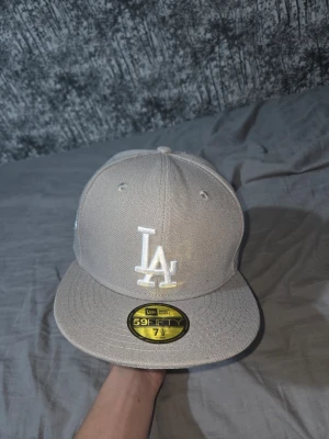Beige LA keps från New Era - Säljer en beige 59FIFTY keps från New Era med LA Dodgers-logga broderad i vitt framtill och en patch på sidan. Klassisk flat brim och strukturerad passform. Perfekt för dig som vill ha en stilren och sportig look.