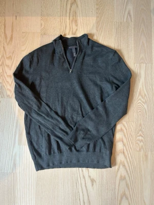 Mörkgrå ziptröja från H&M - Snygg mörkgrå tröja från H&M i slim fit-modell med halv dragkedja vid halsen. Tillverkad i mjukt material som passar perfekt till lager på lager. Tröjan har långa ärmar och ribbade muddar vid ärmslut och nederkant.