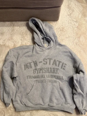 Gymshark hoodie med tryck, storlek L (M) - Snygg Gymshark hoodie i storlek L. Upplevs mindre i storleken så passar M. Hoodien har en känguruficka framtill. Förvarad i ett djur- och rökfritt hem, knappt använd. Köpt i herrarnas sektion, men kan användas av båda könen för både gym/chill. 