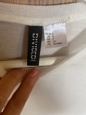 Vit t-shirt från Divided H&M - Klassisk vit t-shirt från Divided H&M i storlek S. T-shirten har rund halsringning och korta ärmar. Tillverkad i ett mjukt och tunt material som känns skönt mot huden. Enkel och stilren design som passar till allt.