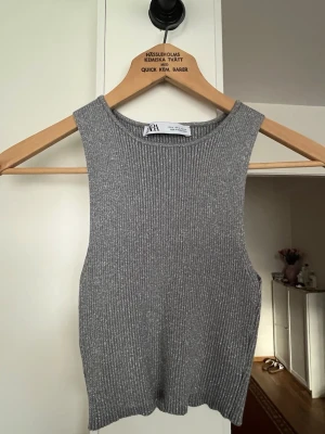 Grå ribbad linnetopp från Zara - Säljer en grå ribbad linnetopp från Zara. Toppen är ärmlös och har en croppad passform med rund halsringning. Perfekt att styla med höga jeans eller kjol för en trendig look.