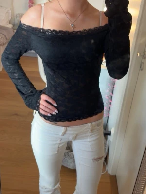 Svart offshoulder spetsblus - Snygg svart offshoulder-blus i spets med långa ärmar och fina spetsdetaljer längs kanterna.