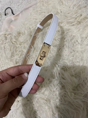 Vitt smalt bälte i pu - Snyggt och stilrent vitt bälte i smalt utförande. Bältet har en enkel design med justerbar längd och diskret spänne i metall. Perfekt för att lyfta vilken outfit som helst och passar till både jeans och klänning.