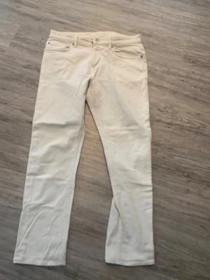 Vita jeans  - Säljer ett par stilrena beiga jeans med rak passform och klassisk femficksdesign. Jeansen är tillverkade i mjuk bomull och har bälteshällor samt knappgylf. Perfekta för dig som vill ha en clean och enkel look.
