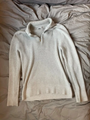 Ljusgrå stickad tröja med quarterzip  - Ljusgrå stickad tröja med quarterzip och hög krage. Tröjan har ribbstickad struktur, långa ärmar och en avslappnad passform. Perfekt för lager på lager och enkel att styla till olika outfits. MODELLEN ÄR 181 CM