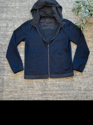 Massimo Dutti cardigan  - Säljer en snygg och stilren mörkblå cardigan från Massimo Dutti i storlek S. Modellen har dragkedja framtill, två sidfickor samt avtagbar luva, vilket gör den både praktisk och lätt att variera efter väder och stil. Passar perfekt som vår, sommar eller höstjacka och fungerar lika bra till vardags som för en mer uppklädd look.