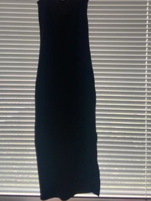 Svart långklänning med slits - En enkel och stilren svart långklänning i figurnära modell. Klänningen är ärmlös och har en slits på sidan för extra rörelsefrihet. Perfekt för dig som gillar minimalistisk stil och vill ha en klassisk bas i garderoben.