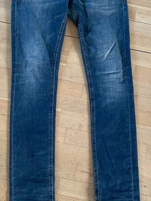 Dondup George jeans - Säljer ett par blå jeans med rak passform och lätt slitna detaljer. Jeansen har klassisk femficksdesign och är tillverkade i denim med snygg tvätt. Perfekta till en avslappnad stil och passar till det mesta.