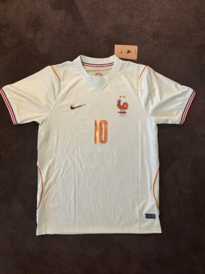 Frankrike borta VM 26/27 borta Mbappe 10 - OBS ! Tröjan ser lite konstig ut pga ljuset skriv privat för mer bilder.                                                       Fotbollströja med Mbappe på ryggen. Tröjan är helt ny med tagg kvar och i perfekt skick. Perfekt för dig som är supporter, samlar på fotbollströjor eller vill ha en snygg tröja till träning och vardag.                                                      ⚪ Skickas inom 24 timmar Vid intresse eller frågor är det bara att skicka 👍