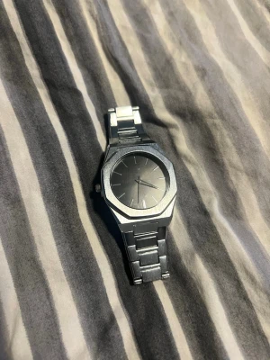 Stilren silverfärgad klocka - Snygg och minimalistisk klocka i silverfärgad metall med länkarmband och rund urtavla utan siffror. Klockan har en modern design med borstade detaljer och passar perfekt till dig som gillar en clean look. 21,5cm, Vid frågor är det bara att höra av sig. Helt ny, aldrig använd. 