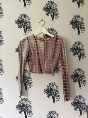 Brun tie-dye croppad långärmad topp - Trendig croppad topp med lång ärm i brun och beige tie-dye. Tunn och stretchig, perfekt för lager på lager eller som statement piece. Snygg passform med rund halsringning och coolt mönster.