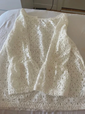 Vit spetsblus med blommönster - Säljer en söt vit blus i spets med blommigt mönster. Blusen är ärmlös och har en rund halsringning. Perfekt för dig som gillar romantisk och feminin stil. Passar till både jeans och kjol!