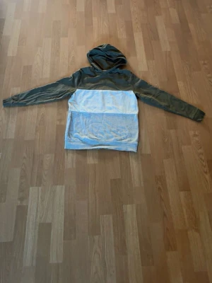 Grön och grå hoodie med huva - Säljer en stilren hoodie i två färger, med mörkgrön överdel och ärmar samt ljusgrå nederdel. Hoodien har en klassisk huva och långa ärmar. Perfekt för dig som gillar en enkel men snygg look. Materialet känns mjukt och bekvämt.