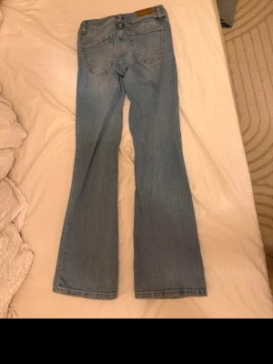 Ljusblå bootcut jeans - Säljer ett par ljusblå bootcut jeans med klassisk femficksdesign och lågmidja. Jeansen har en lätt utsvängd passform nedtill och är tillverkade i denim. Perfekta för en avslappnad och trendig look.