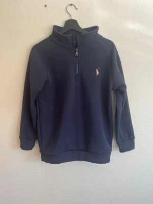 Mörkblå quarter zip hoodie Polo - Säljer en mörkblå hoodie från Polo Ralph Lauren med quarter zip och klassisk broderad logga på bröstet. Tröjan har hög krage, ribbade muddar och är tillverkad i mjukt bomullsmaterial. Perfekt för dig som gillar stilren och sportig look. (obs ej orginal) 
