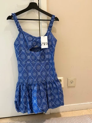  Ny populärt Blå kortklänning med blommigt med volang med prislapp på  - Supersöt blå kortklänning med vita blommor och rutmönster. Klänningen har breda axelband, twistad detalj framtill och en liten cut-out under bysten. Kjolen är volangig och ger en lekfull vibe. Perfekt för varma dagar och sommarhäng!