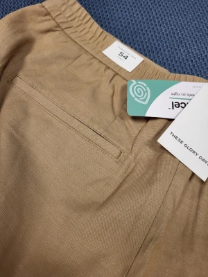 Beige mjukisbyxor från These Glory Days 54 L - Säljer ett par beige mjukisbyxor från These Glory Days. Byxorna har resår i midjan, raka ben och diskreta fickor både fram och bak. Tillverkade i ett mjukt och bekvämt material som passar perfekt för en avslappnad stil.