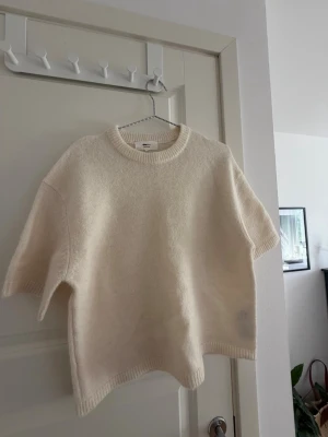 Vit stickad tröja Gina Tricot - Säljer en vit stickad tröja från Gina Tricot i ullblandning. Tröjan har korta ärmar, rund halsringning och ribbade kanter. Enkel och stilren design som passar perfekt till lager på lager eller som ett statement-plagg.