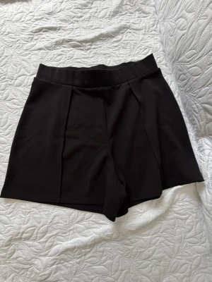 Svarta shorts från H&M, midwaist - Snygga svarta shorts från H&M i midwaist-modell. De har en enkel och stilren design med bred linning och lätt utsvängda ben. Materialet är mjukt och stretchigt, perfekt för varma dagar. Passar till många olika outfits!