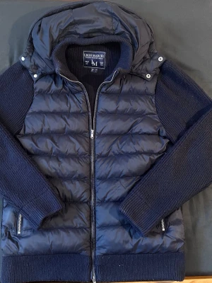 Cardigan Leon Marcél - Mörkblå cardiganjacka från Leon Marcél med vadderad framsida i nylon och vadderade ärmar och rygg i bomull, ull och kaschmir. Stilren och fräsch jacka som passar bra både till vår och sommarkvällar. Avtagbar luva.  Hör av dig vid minsta fråga eller fundering! Ärlig säljare som skickar snabbt. 