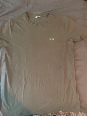 Mörk grå t-shirt från Lacoste - Snygg mörk grå t-shirt från Lacoste med den klassiska broderade krokodilloggan på bröstet. T-shirten har rund halsringning och korta ärmar. Perfekt basplagg för en clean och stilren look.