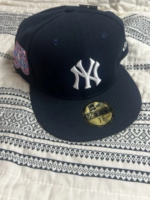 New Era Yankees svart 59Fifty keps, olika snapbacks - Säljer en svart New Era 59Fifty keps med New York Yankees-logga broderad i vitt framtill och World Series-märke på sidan. Klassisk rak skärm och hög krona. Kepsen är i ett robust material och har officiella etiketter kvar. Perfekt för dig som gillar streetwear och sportig stil. 