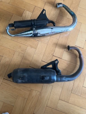 Två avgassystem till moped - Säljer två avgassystem till moped, ett i krom med svart värmesköld och ett i svart metall. Båda har fästen och böjda rör. Perfekt för dig som vill byta eller uppgradera din moppe. 700 för mk1 o 300 för org rör