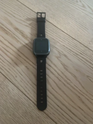 Svart smartklocka med silikonarmband - Snygg svart smartklocka med fyrkantig display och mjukt silikonarmband. Klockan har en modern design med slät ram och flera hål för justerbar passform. Perfekt för dig som vill ha koll på notiser och aktivitet direkt på handleden.