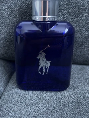 Ralph Lauren Polo Blue parfym - En stilren parfymflaska från Ralph Lauren Polo Blue med djupblått glas och silverfärgat lock. Flaskan har den klassiska polospelaren i silver på framsidan. Perfekt för dig som gillar exklusiva och sportiga dofter.Flaskan är 75 ml men jag har använt den väldigt lite och den kommer inte till användning så därför säljer jag det. Finns markerat på en bild hur mycket den använts.