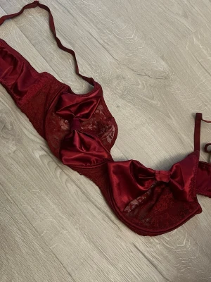 Vinröd spets-bh med rosetter Nelly - Snygg vinröd bh från Nelly med spetsdetaljer och stora satängrosetter framtill. Bh:n har justerbara axelband och hakknäppning bak. Materialet är en mix av spets och satin som ger en lyxig känsla.