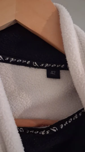 Vit fluffig tröja  - Vinter tröjai storlek 42. Tillverkad i mjukt och fluffigt material som känns skönt mot huden. Perfekt för att slappa hemma och hålla sig varm. Klassisk design med huva och kontrasterande detaljer på insidan.