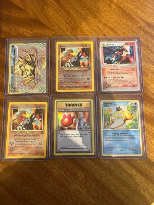 Pokémonkort samling i plastfickor - Säljer ett set med sex Pokémonkort i genomskinliga plastfickor. Bland korten finns Entei, Blaziken ex, Psyduck, Gym Badge-tränarkort och två holografiska kort. Perfekt för samlare eller Pokémonfans som vill utöka sin samling.