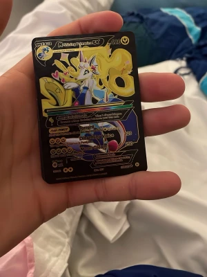 Pokémonkort Mega Shining Primarina EX - Unikt Pokémonkort med Mega Shining Primarina EX-motiv. Kortet har en glansig svart och gul design med färgglada detaljer och text på engelska. Perfekt för samlare eller Pokémonfans som vill utöka sin kortsamling.