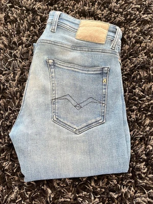 Ljusblå Replay jeans med tvättad look - Snygga ljusblå jeans från Replay med tvättad effekt och klassisk femficksmodell. Jeansen har en diskret logga på bakfickan och patch i beige vid linningen. Perfekta för en avslappnad och trendig stil. Hör av er vid funderingar! 
