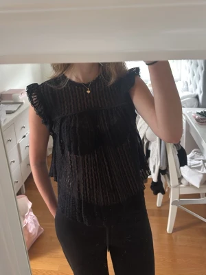 Svart spetsig blus med volanger - Svart jättefin spetsig topp med fin detalj i ryggen från Nelly. Storlek S. Den är aldrig använd men saknar prislappen.