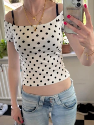 Vit prickig offshoulder topp - Snygg vit offshoulder topp med svarta prickar och croppad passform. Toppen har korta ärmar och sitter tight mot kroppen. Perfekt för dig som gillar trendiga och lekfulla plagg. Använd endast en gång så precis som ny!💕💕💕