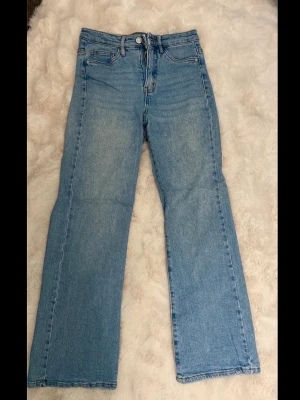 Ljusblå raka jeans - Säljer ett par ljusblå jeans med rak passform och klassisk femficksdesign. Jeansen har hög midja och är tillverkade i ett slitstarkt denimtyg. Perfekta för en avslappnad och trendig look.