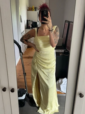 Gul långklänning med slits från Azazie - Superfin citrongul klänning från Azazie! Perfekt nu inför bal och bröllop!  Säljer denna superfina klänning då de blev en annan modell för min del, så klänningen är endast testad!  Glidskydd på axlarna, både kedja och superfin  knytning i ryggen! Klänningen är satin stretch samt färg citrongul! Medföljer väska till klänningen så att den kan hänga i garderoben skyddad, eller ta med säkert på resa!  ❌ Klänningen på bilden är strl 40 ❌  Ordinarie pris 1299:-
