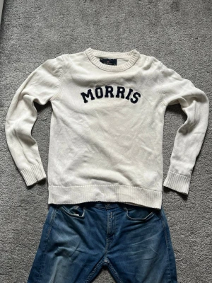Vit stickad tröja från Morris - Vit stickad tröja från Morris med rund halsringning och svarta bokstäver broderade över bröstet. Tröjan har ribbade muddar vid ärmslut och nederkant. Perfekt för en avslappnad och stilren look.