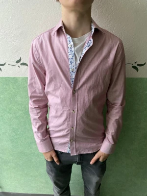 Rosa skjorta från Riley med blommigt foder - Snygg rosa skjorta från Eton med lång ärm och blommigt mönstrat foder på insidan av kragen och knappslån. Skjortan har klassisk krage, knappar framtill och en slim passform. Perfekt för dig som vill sticka ut lite extra.