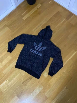 Mörkblå Adidas hoodie med logga - Säljer en mörkblå hoodie från Adidas med stor vit logga på bröstet. Hoodien har långa ärmar, huva och ribbade muddar vid ärmslut och nederkant. Perfekt för en chill och sportig look.