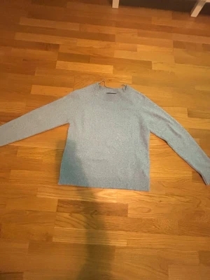 Ljusblå stickad tröja Vero Moda - Ljusblå stickad tröja från Vero Moda med rund halsringning och långa ärmar. Tröjan har en enkel, klassisk design med ribbade muddar vid ärmslut och nederkant. Perfekt för lager på lager och en chill vardagslook.