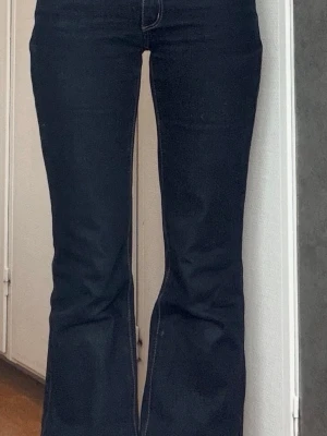 Mörkblå bootcut jeans - Snygga mörkblå bootcut jeans med klassisk femficksdesign och kontrastsömmar. Jeansen har en hög midja och utsvängda ben, vilket ger en retrovibe. Tillverkade i stretchigt denimtyg för skön passform.