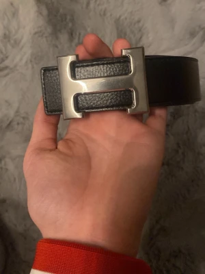 Svart skärp med stor silverspänne - Snyggt svart skärp i skinn med ett stort, rektangulärt silverspänne som har en modern design. Perfekt för att lyfta vilken outfit som helst och ger en clean look. Passar till jeans eller kostymbyxor.