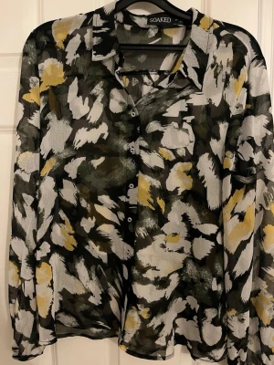 Mönstrad transparent skjorta Soaked - Snygg transparent skjorta från Soaked med abstrakt mönster i svart, vit, grå och gul. Skjortan har klassisk krage, knappar framtill och lång ärm. Perfekt för dig som gillar statement-plagg och vill sticka ut lite extra.