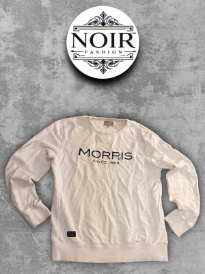 Vit sweatshirt från Morris - Snygg vit sweatshirt från Morris med tryckt logga och text 'Morris Since 1968' på bröstet. Tröjan har rund halsringning, långa ärmar och ribbade muddar vid ärmslut och nederkant. Perfekt för en clean och stilren look.