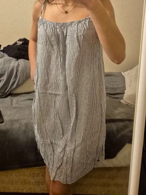 Randig sommarklänning med smala axelband - Luftig kortklänning med smala axelband och tunna vertikala ränder i vitt och blått. Klänningen har en rak passform som kan stylas både löst och mer figurnära. Perfekt för varma dagar och enkel att matcha med accessoarer. Materialet känns lätt och svalt. Står ej storlek, men jag bär vanligtvis S så skulle gissa på L kanske. Men om man vill kan man göra den mindre som på bild 2 och sy om den till sin egna storlek. 