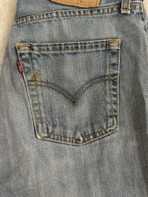 Levi's ljusblå slitna jeans - Ljusblå jeans från Levi's med klassisk femficksdesign och bootcut. Jeansen har slitningar och hål vid knäna för en trendig, avslappnad look. Tillverkade i bomull med den ikoniska röda Levi's-lappen på bakfickan.