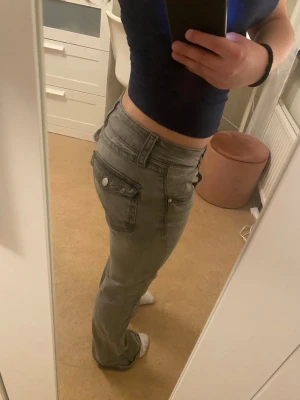 Grå bootcut jeans med fickdetaljer - Lite missfärgning på vissa ställen men ingenting som man tänker på. gråa bootcut jeans med låg midja och snygga fickdetaljer på sidorna. Jeansen har klassisk femficksdesign och knäppning med knapp och dragkedja. Perfekta för dig som gillar en avslappnad och trendig look. 
